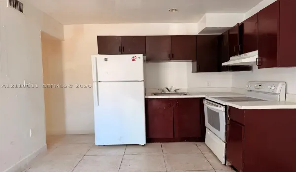 Kitchen featuring dark cabinetry, white laminate countertops, tile flooring, and integrated white appliances