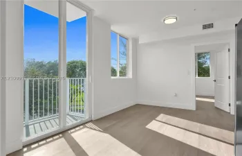 Floor-to-ceiling glass sliding doors, private balcony with white railing, wood-finish flooring, and recessed ceiling lighting