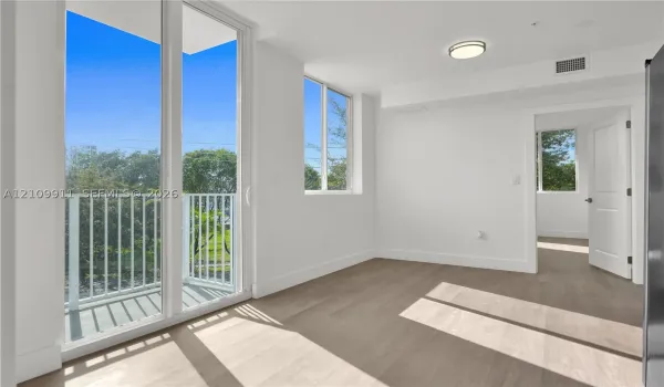 Floor-to-ceiling glass sliding doors, private balcony with white railing, wood-finish flooring, and recessed ceiling lighting
