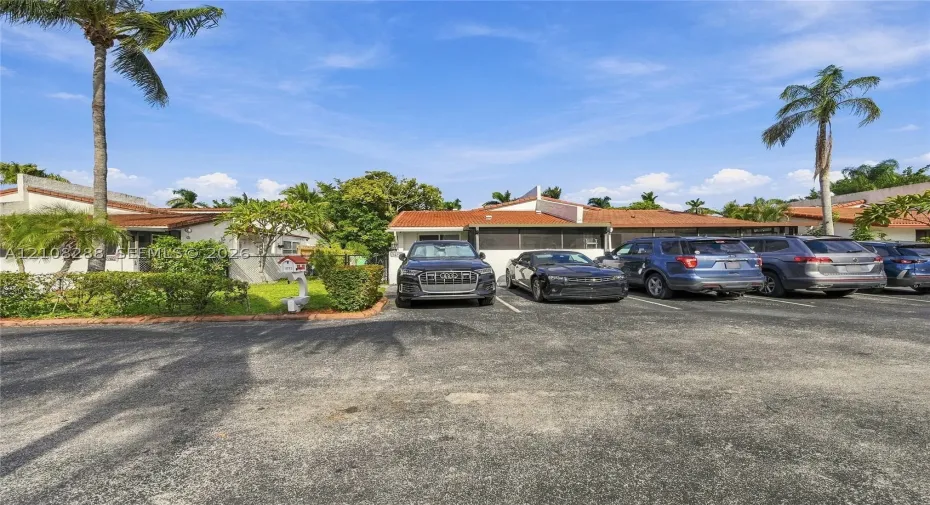 Single-story exterior featuring a clay tile roof, paved off-street parking, and established landscaping with mature palm trees