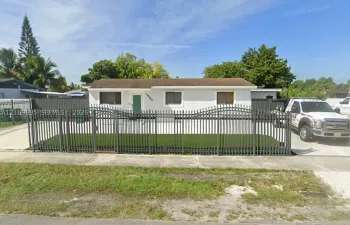 Single-story residence featuring a light-colored stucco exterior, decorative metal front fencing, and a concrete driveway