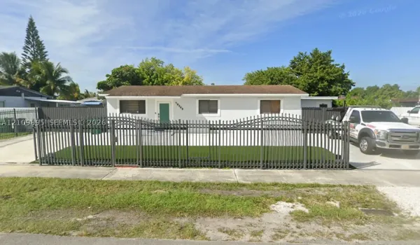 Single-story residence featuring a light-colored stucco exterior, decorative metal front fencing, and a concrete driveway