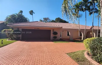 Stucco exterior featuring a clay tile roof, arched covered entry, paver driveway, and mature landscaping