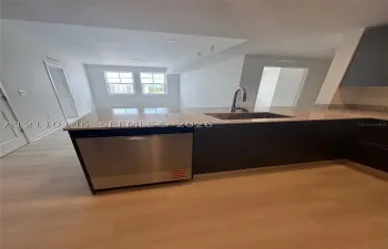 Kitchen featuring a stone-composite countertop, stainless steel dishwasher, undermount stainless steel sink with a high-arch faucet, flat-panel dark cabinetry, and light-toned wood-finish flooring