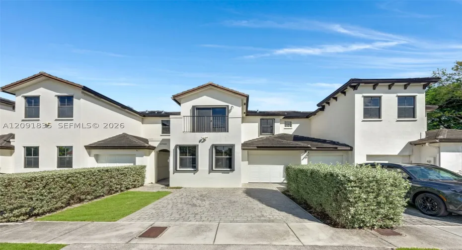 Stucco exterior featuring multiple attached garage bays, a paved driveway, and an upper-level balcony with metal railings