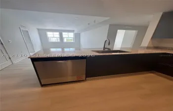 Kitchen featuring a stone-composite countertop, stainless steel dishwasher, undermount stainless steel sink with a high-arch faucet, flat-panel dark cabinetry, and light-toned wood-finish flooring