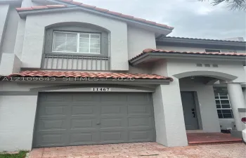 Stucco exterior featuring terracotta-style roof tiles, arched architectural detailing, a paneled garage door, and a covered entryway with column support