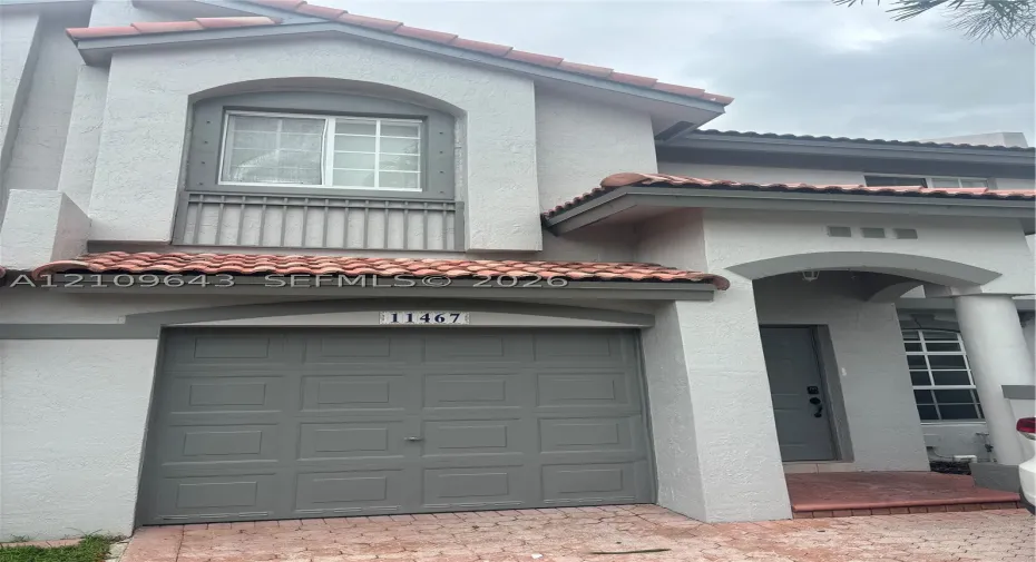 Stucco exterior featuring terracotta-style roof tiles, arched architectural detailing, a paneled garage door, and a covered entryway with column support