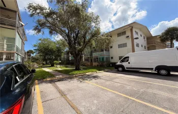 Multi-story exterior featuring a paved parking area with numbered stalls, concrete walkways, screened-in balconies, and mature landscaping