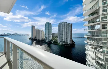 Covered balcony with glass-paneled railing overlooking the waterfront and cityscape