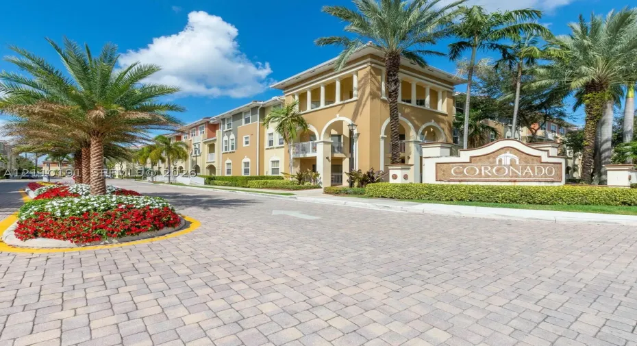Stucco exterior featuring arched architectural detailing, paved stone driveway, and established tropical landscaping