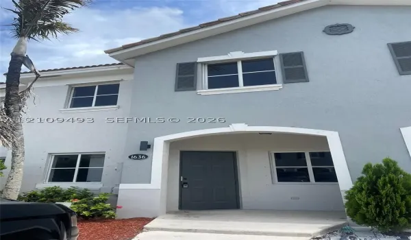 Exterior featuring a light-toned stucco facade, arched entryway, decorative window shutters, and a covered porch