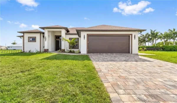 Single-story exterior featuring a neutral stucco facade, multi-textured siding, a paved stone driveway, a deep-set covered entryway, and an attached two-car garage