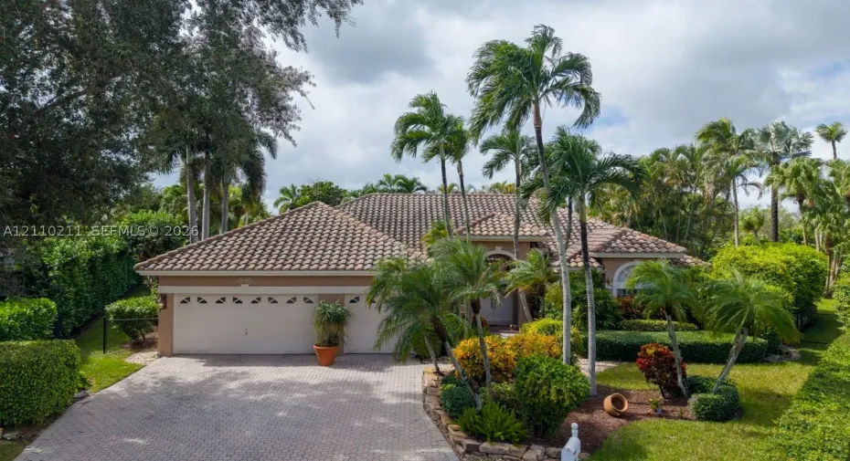 Single-story residence featuring a tile roof, paver driveway, multi-car garage, and mature landscaping