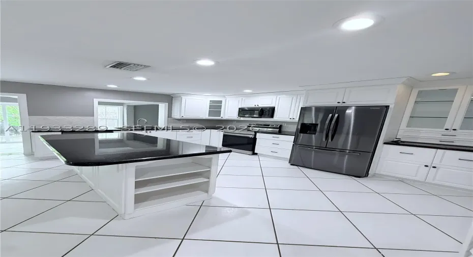Kitchen featuring white cabinetry, an island with stone-finish countertop, stainless steel appliances, glass-front upper cabinets, and tile flooring