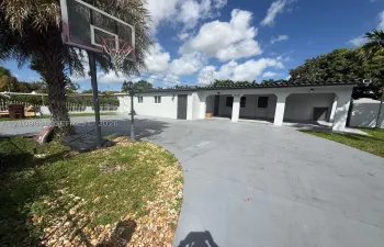 Exterior facade featuring a covered carport, smooth stucco finish, barrel-tile roofline, and an expansive paved driveway