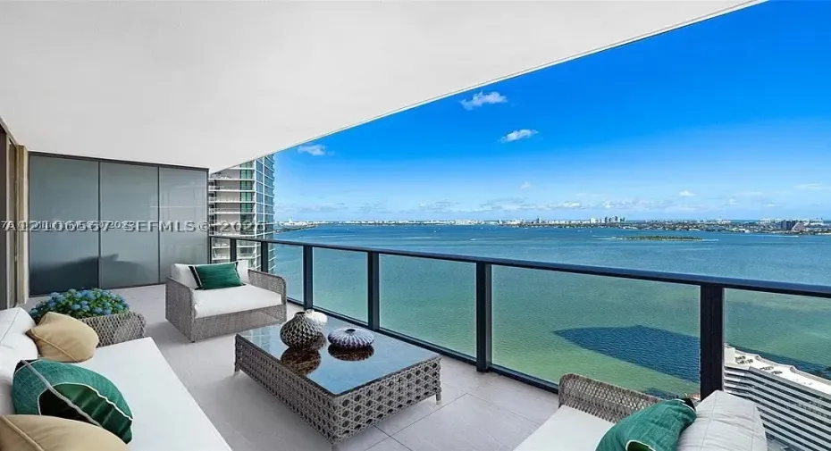 Covered balcony featuring neutral tile flooring, glass panel railings with dark metal framing, and extensive water exposure