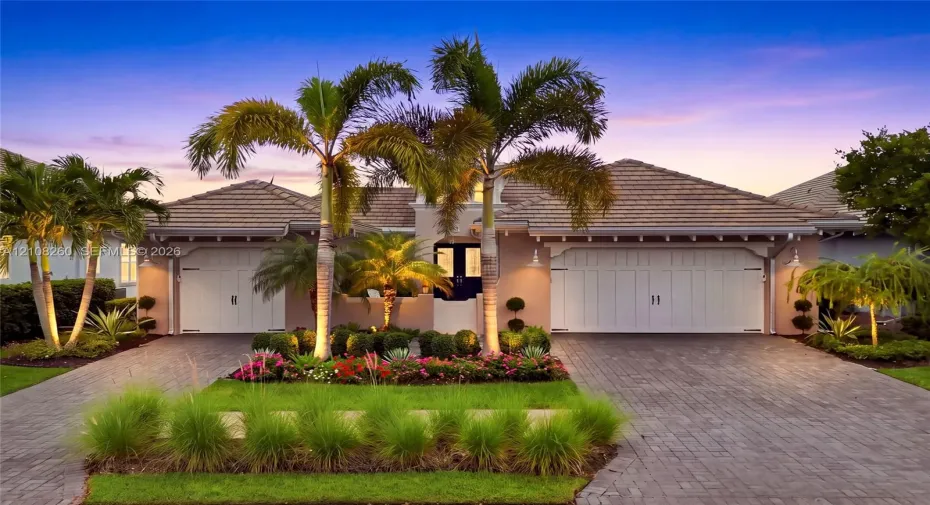 Exterior facade featuring a tile roof, two-car garage, paver driveway, and mature landscaping