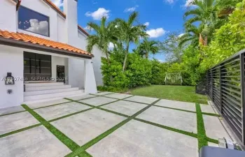 Exterior facade featuring white stucco walls, clay tile roofing, concrete paver patio with turf ribbon accents, and horizontal slat perimeter fencing