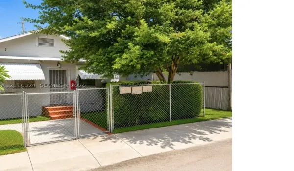Single-story residence featuring a chain-link fenced front perimeter, concrete walkway, mature tree, and exterior metal window awnings
