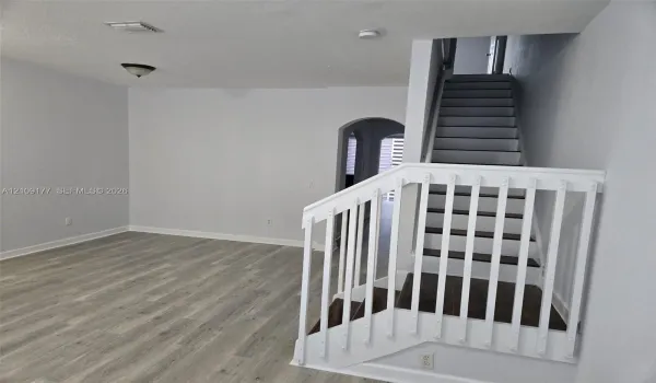Interior area featuring wood-finish flooring, a white-railed staircase, and an arched entryway