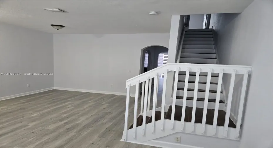Interior area featuring wood-finish flooring, a white-railed staircase, and an arched entryway