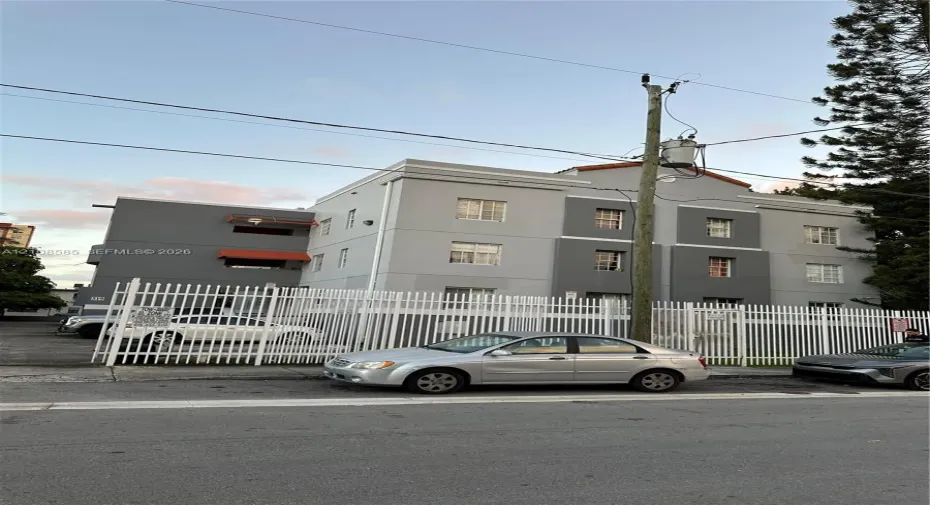 Multi-story exterior featuring a grey stucco facade with color-blocked detailing, multi-pane windows, and a perimeter fence enclosing the property