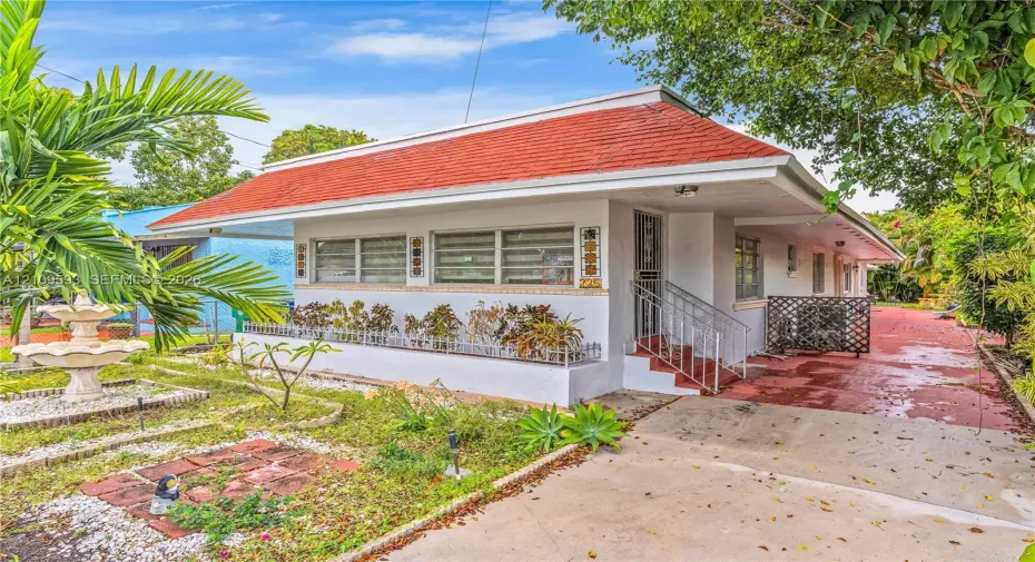 Single-story residence featuring a low-pitched roof, white stucco exterior, integrated planter box, metal security screen door, and a paved driveway