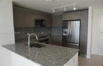 Kitchen featuring stone countertops, flat-panel cabinetry, stainless steel appliances, a single-basin undermount sink, and track lighting