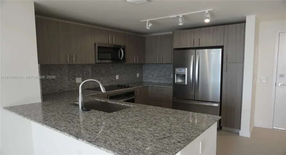 Kitchen featuring stone countertops, flat-panel cabinetry, stainless steel appliances, a single-basin undermount sink, and track lighting