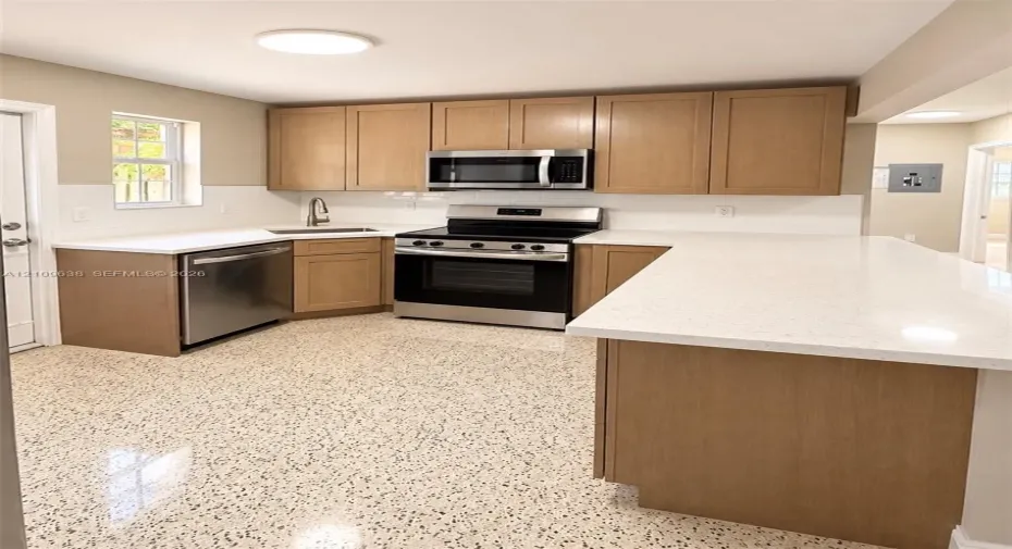 Kitchen featuring light-finish cabinetry, white solid-surface countertops, a full-height tile backsplash, stainless steel appliances, and polished speckled flooring