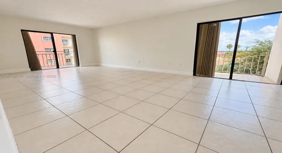 Open-concept living space featuring large-format ceramic tile flooring, neutral wall tones, and two sets of sliding glass doors providing access to exterior balconies