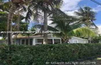 Single-story residence featuring a screened-in porch, light-toned siding, mature palm trees, and dense perimeter landscaping