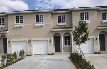 Multi-unit exterior featuring a neutral stucco facade, arched covered entryways with decorative columns, multi-panel garage doors, and grid-pattern window panes