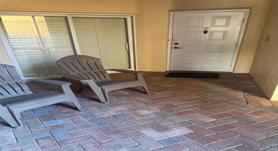 Private patio with herringbone-patterned brick pavers, sliding glass door, and solid-core paneled entry door