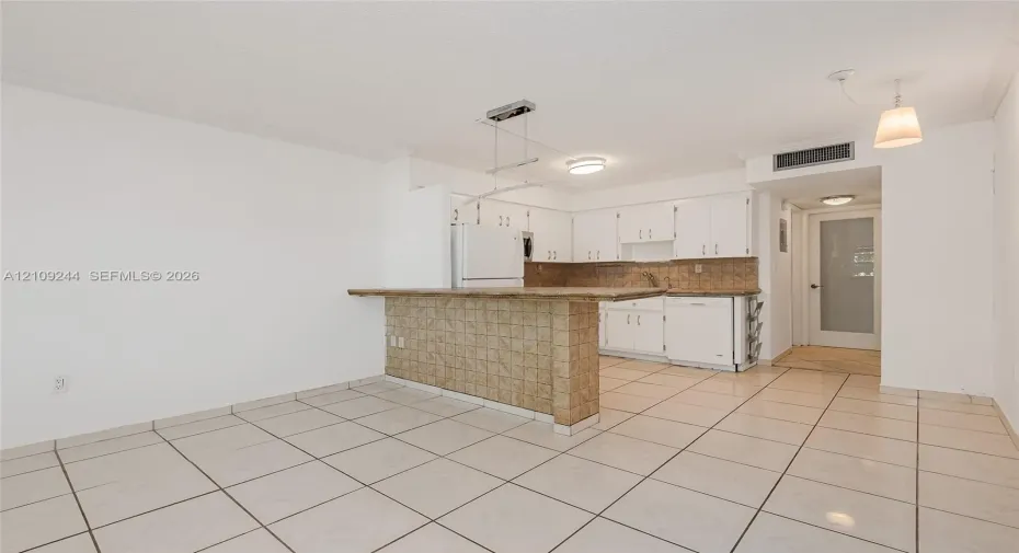Kitchen featuring a tiled breakfast bar, white cabinetry, integrated appliances, and neutral tile flooring