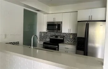 Kitchen featuring white flat-panel cabinetry, light-toned stone countertops, a mosaic tile backsplash, stainless steel appliances, and a gooseneck faucet