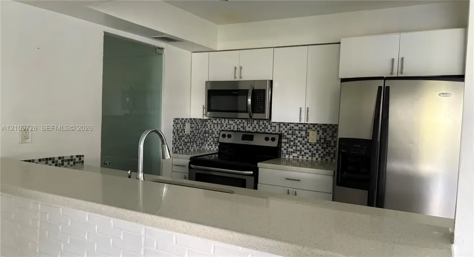 Kitchen featuring white flat-panel cabinetry, light-toned stone countertops, a mosaic tile backsplash, stainless steel appliances, and a gooseneck faucet