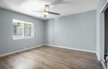 Room featuring wood-finish flooring, light-toned wall paint, a sliding glass window, and a ceiling-mounted light fixture with fan blades