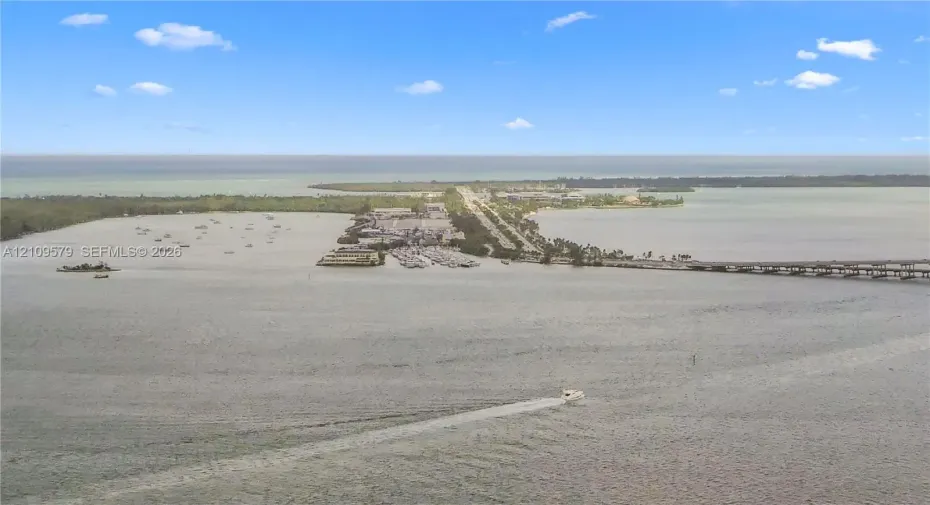 Aerial perspective of coastal landscape featuring expansive open water, a bridge, and a land-based thoroughfare