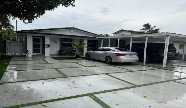 Exterior featuring a paver driveway with turf accents, a covered carport, and a white privacy gate