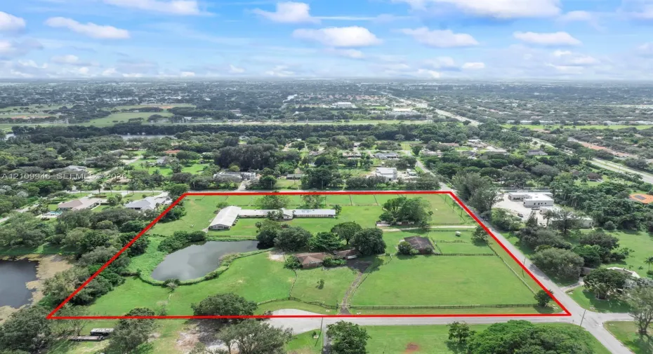 Extensive acreage featuring expansive grassy grounds, a private pond, multiple structures, and perimeter fencing