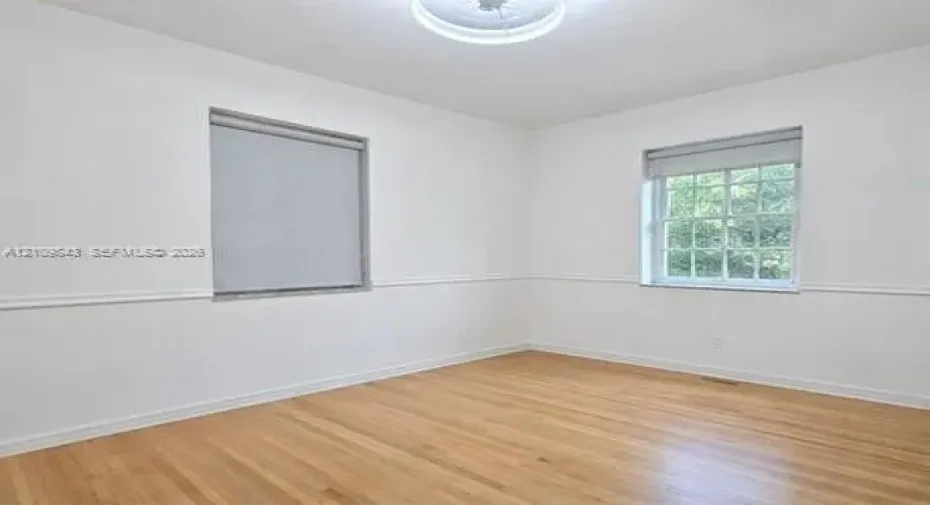 Neutral-toned room featuring wood-finish flooring, white walls with chair rail molding, multi-pane windows, and a central ceiling fixture
