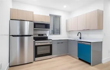 Kitchen featuring wood-finish upper cabinetry, grey lower cabinetry, quartz countertops, stainless steel appliances, and a matte black gooseneck faucet