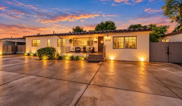 Spanish-style exterior featuring smooth stucco siding, a barrel-tiled roof, an elevated concrete porch with decorative metal railing, a wide concrete driveway, and solid wood-finish fencing