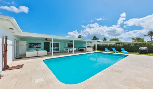In-ground swimming pool with stone-tiled patio, covered lanai, outdoor shower, and perimeter hedging