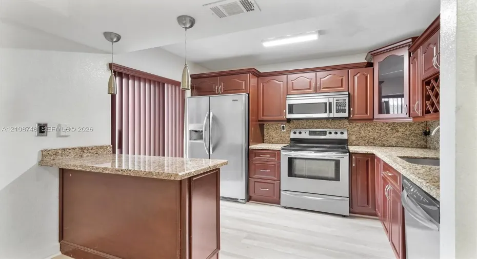 Kitchen featuring wood cabinetry, stone countertops, stainless steel appliances, a built-in wine rack, and two pendant lights