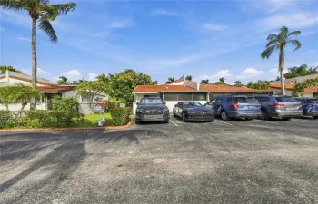 Single-story exterior featuring a clay tile roof, paved off-street parking, and established landscaping with mature palm trees