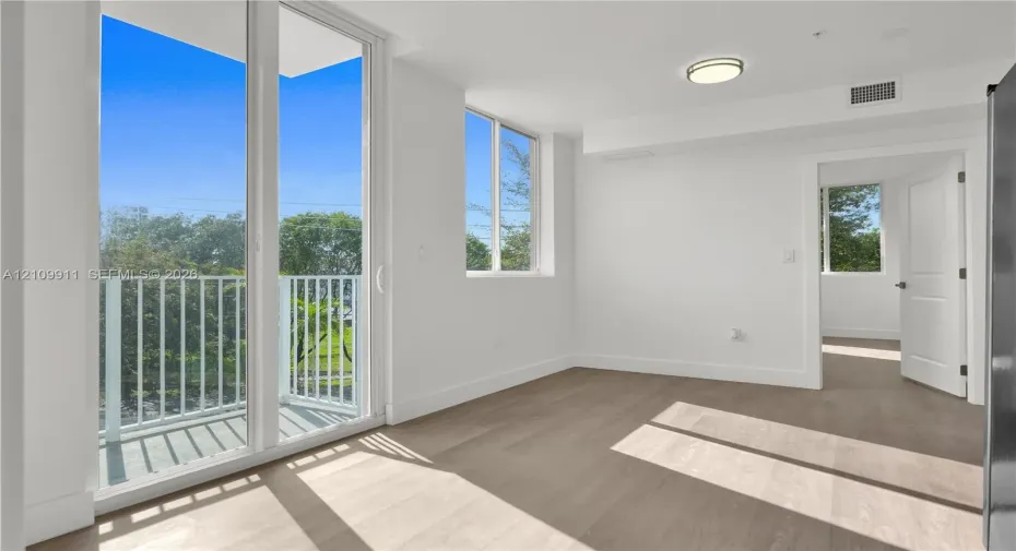 Floor-to-ceiling glass sliding doors, private balcony with white railing, wood-finish flooring, and recessed ceiling lighting