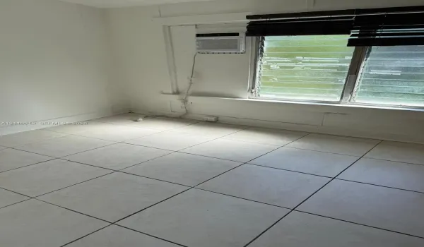 Room featuring light-toned tile flooring, louvered glass windows, and a wall-mounted air conditioning unit
